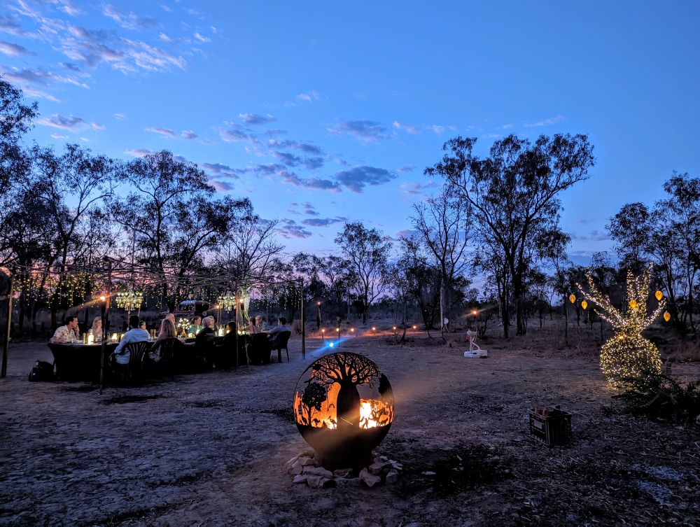 People dining at night under the stars with a fire.
