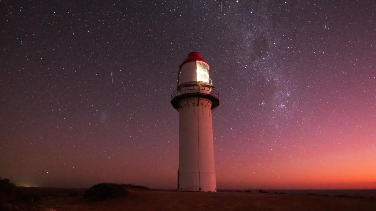 An image of a lighthouse in the dark standing against a starry night. 