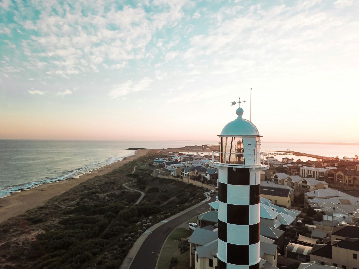 A black and white chequered lighthouse standing tall above residential houses overlooking the ocean. 