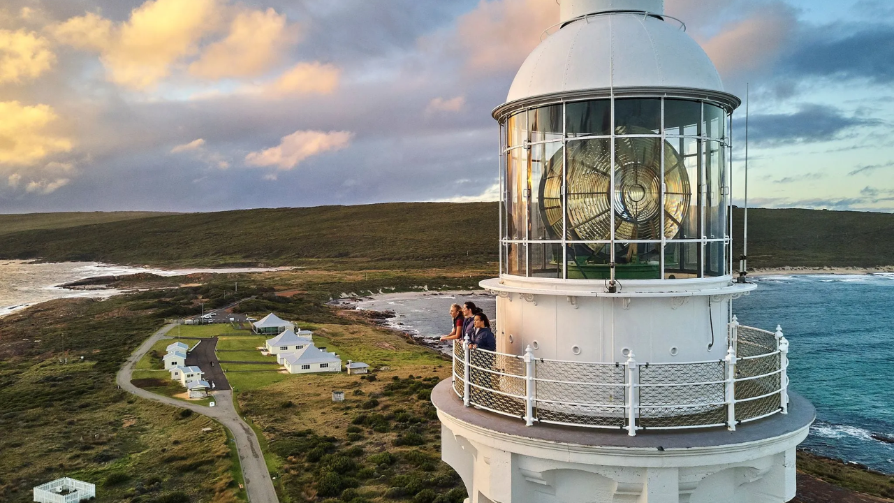 3 women stand at the top of a lighthouse, overlooking the ocean and surrounding landscape.
