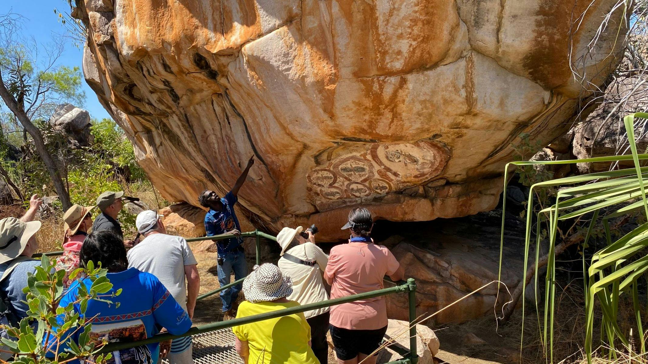 People on a guided tour with an Aborignal person viewing ancient rock art.