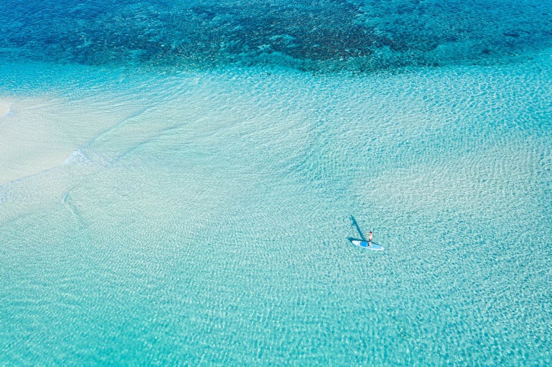 A person paddling on a paddleboard in the middle of a crystal clear bay