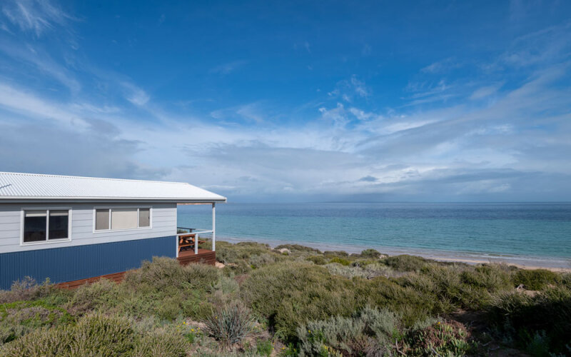 A cabin sitting in the bush in front of the ocean