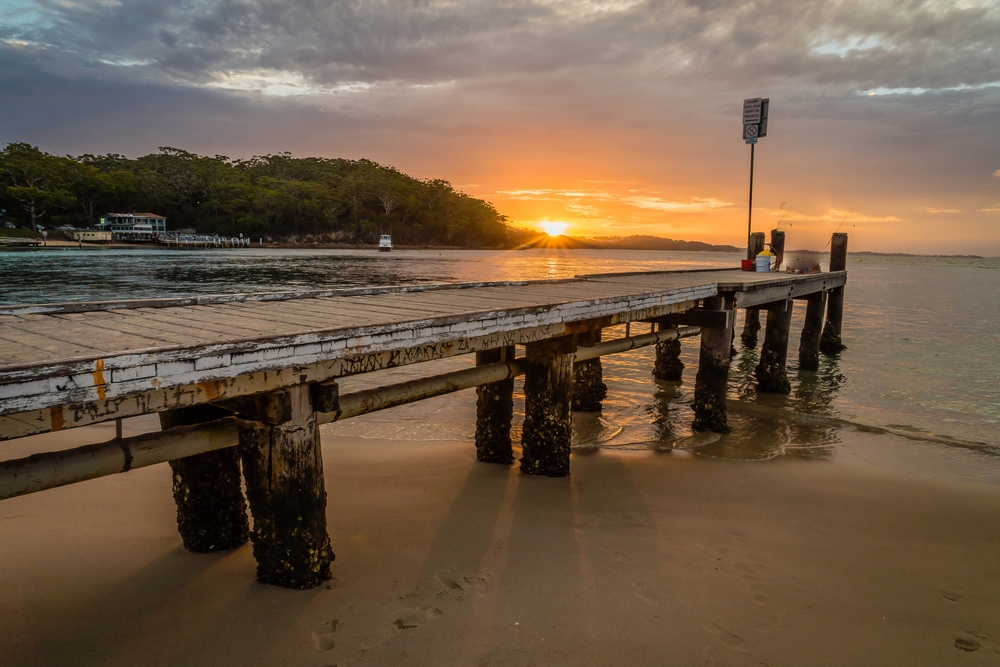 A wooden jetty sits over the ocean with the sunset