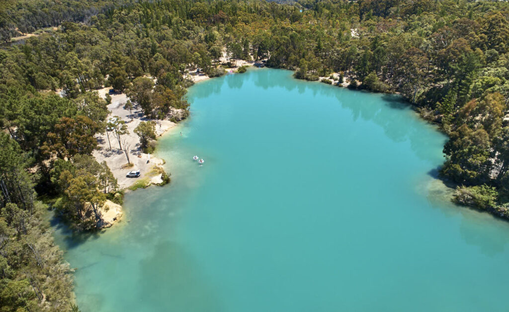An aerial image of a turquoise blue lake surrounded by trees. 