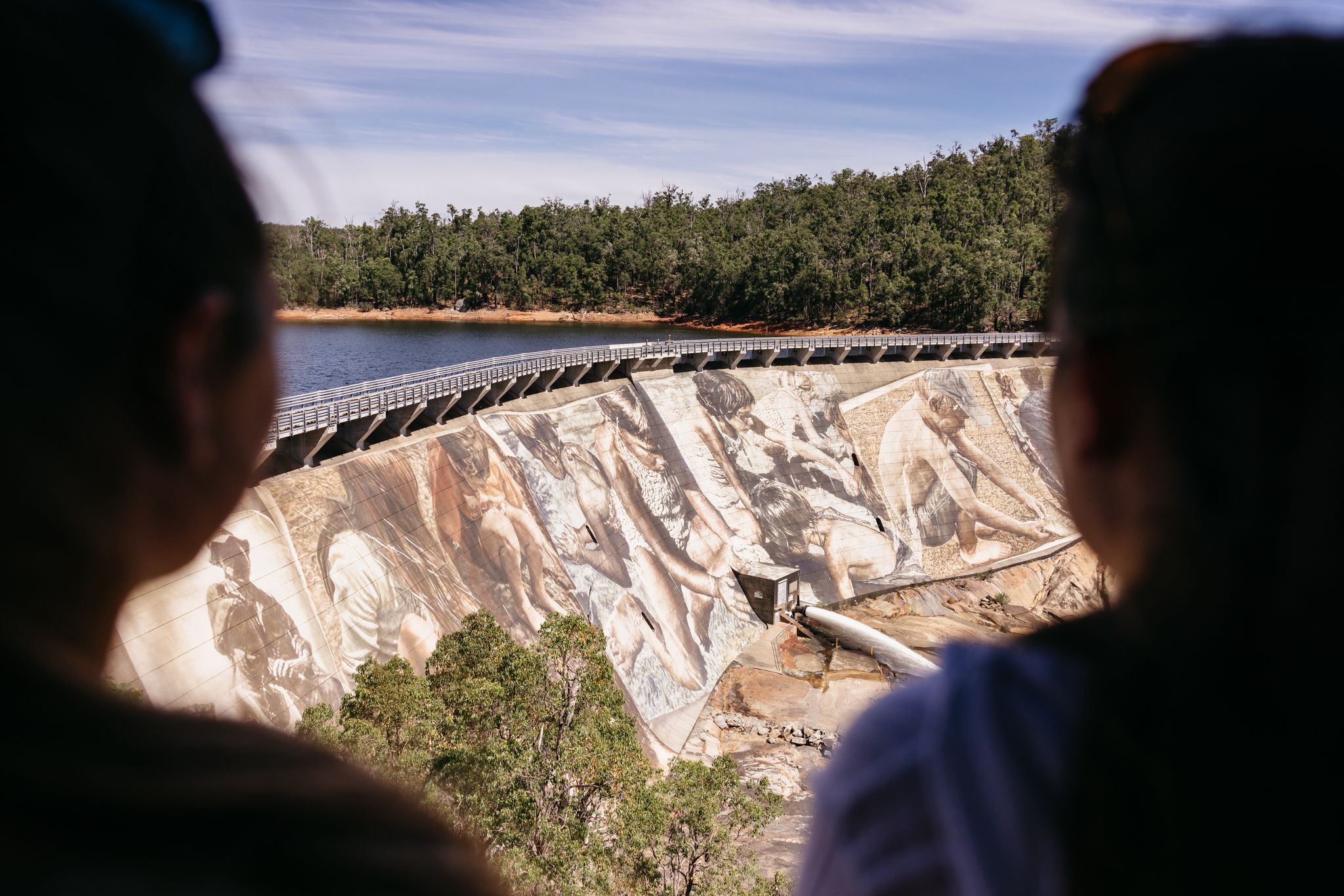people gathered in front of a large dam mural.