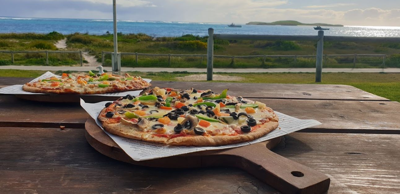 An image of pizzas on a bench in front of the ocean