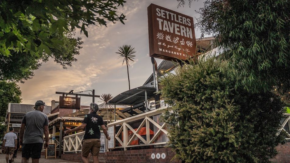 An image of 3 men walking on a pathway outside a tavern