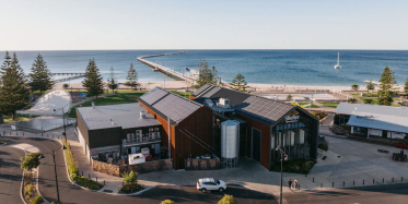 A drone image of a brewery in front of the ocean with a jetty