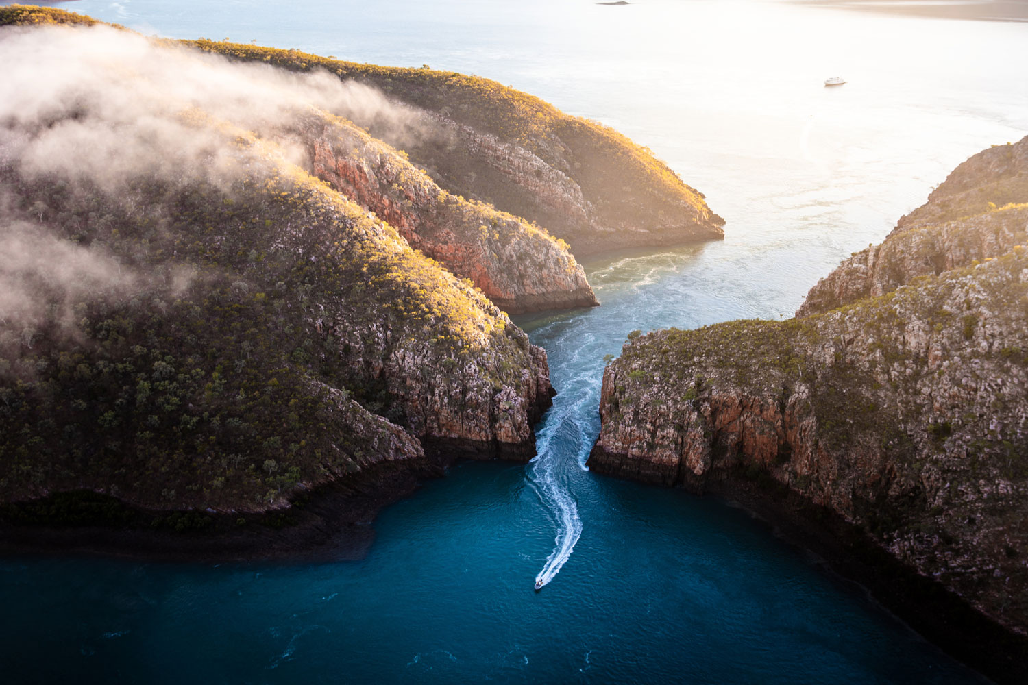 A boat zooming across the water between two huge boulders