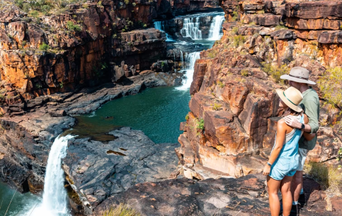 A man and woman stands on top of a mountain above a flowing waterfall