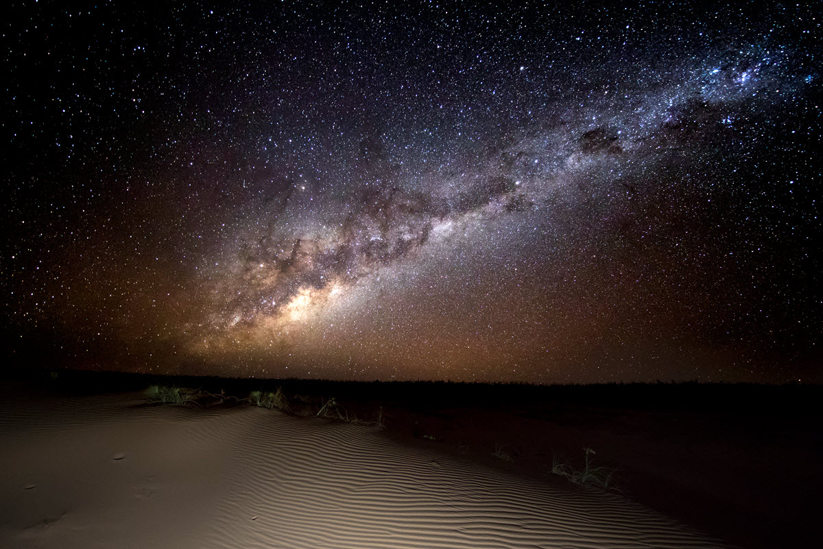A stunning display of light and stars over the sandy shoreline.