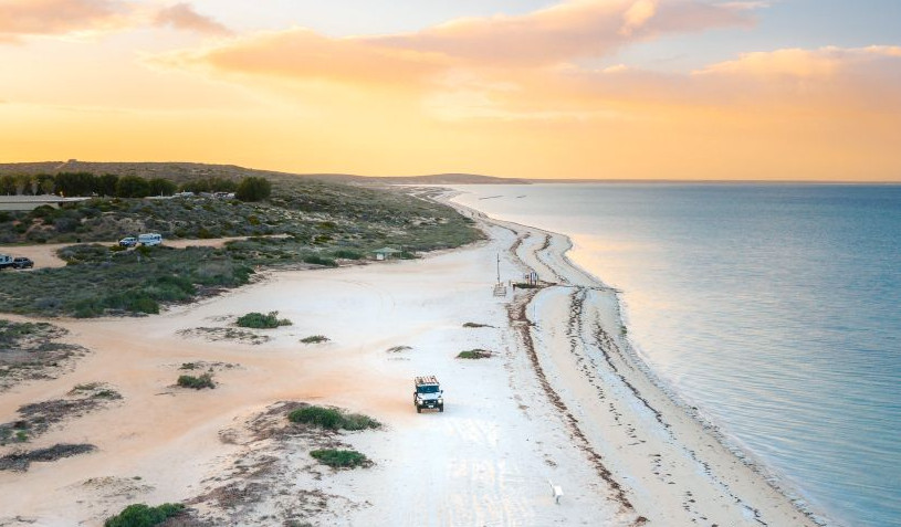 A car drives along a white sandy beach with the ocean on the right side. 