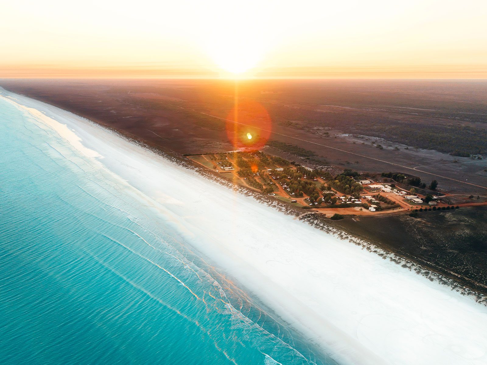 a drone image of a long stretch of white beach with turquoise waters.