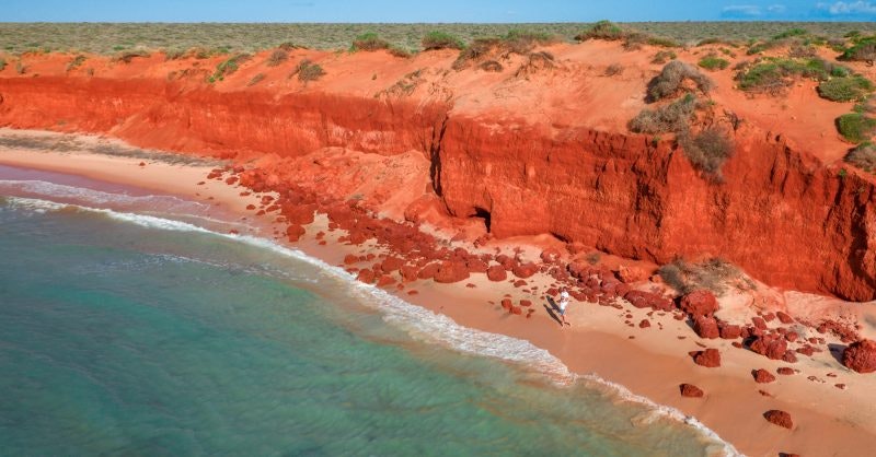 An aerial image of a mountain range with red cliffs, surrounding the ocean