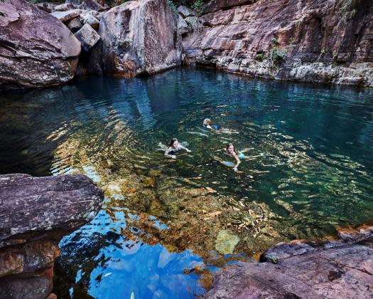 3 children swimming in crystal clear waters in the gorge surrounded by red rock.