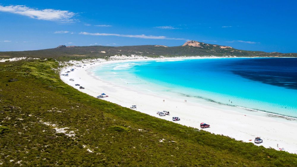 Cars parked on white sandy beach along the water.