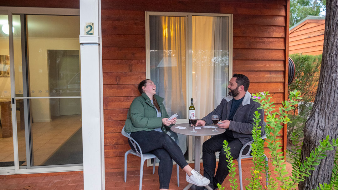 A couple at Margaret River Tourist Park sit outside a cottage enjoying winter down south with a glass of red wine