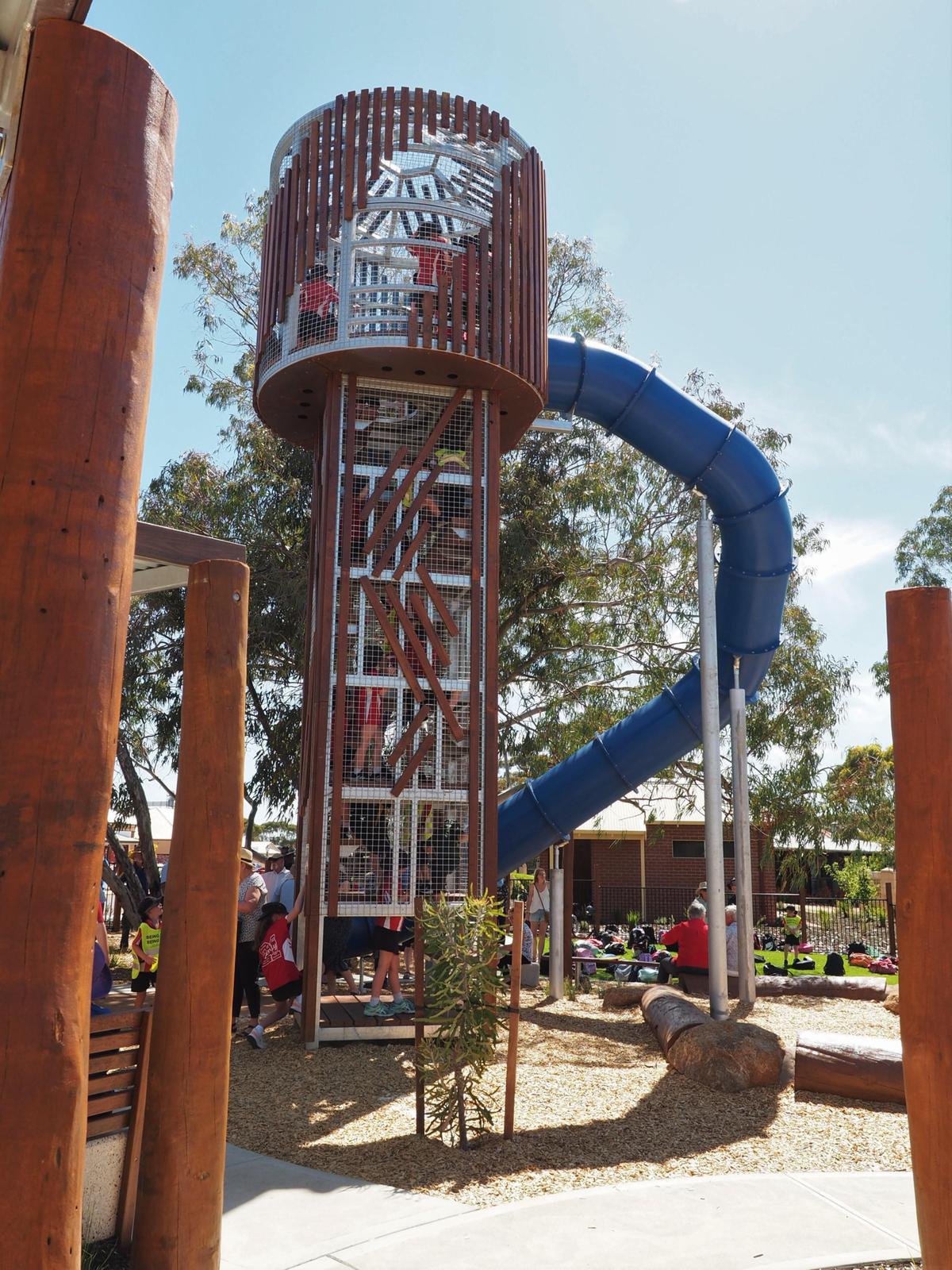 Children climbing on a structure to reach a large blue slide 